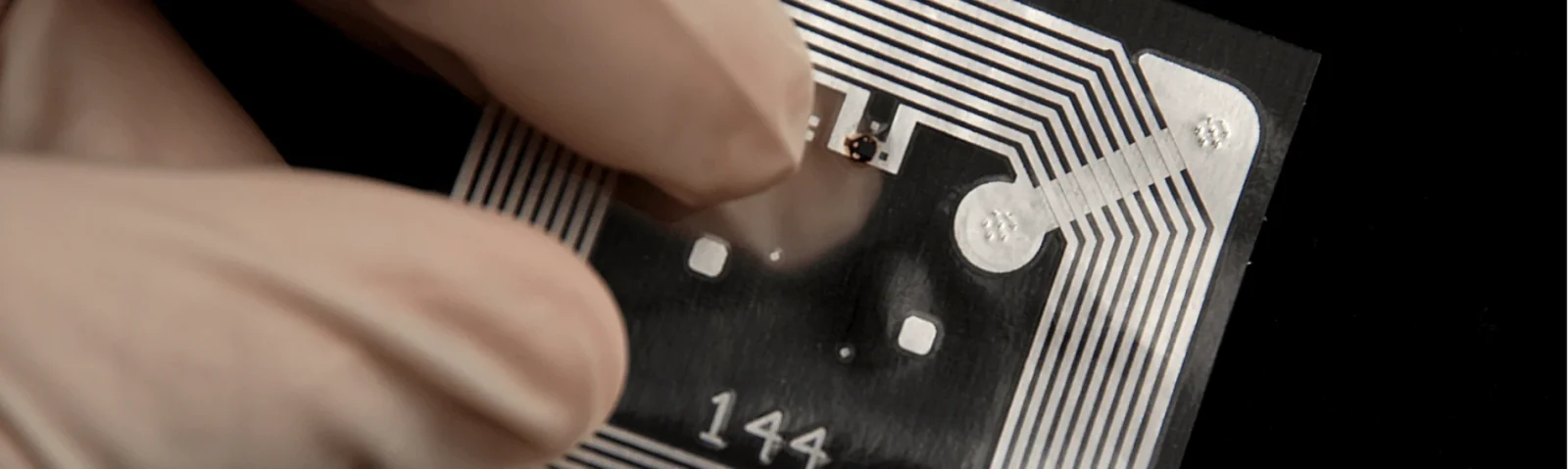 Fingers holding a flexible RFID tag with its printed antenna coil