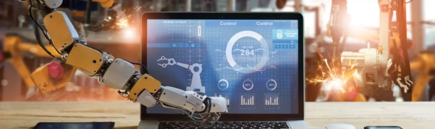 Industrial robot arms beside a laptop showing a production-control dashboard