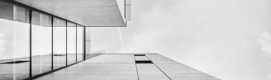 Looking up the glass and concrete facade of a modern office building against an overcast sky