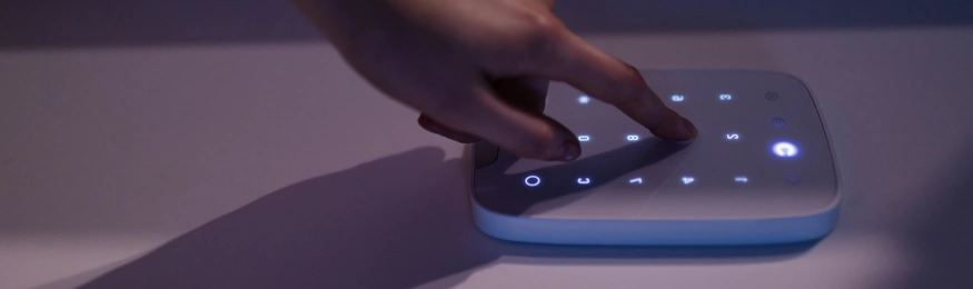 A hand pressing an illuminated touch keypad on a wall-mounted device