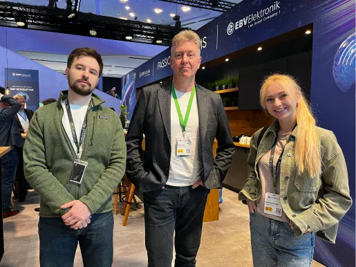 Three attendees with badges standing in front of the EBV Elektronik stand at a trade fair