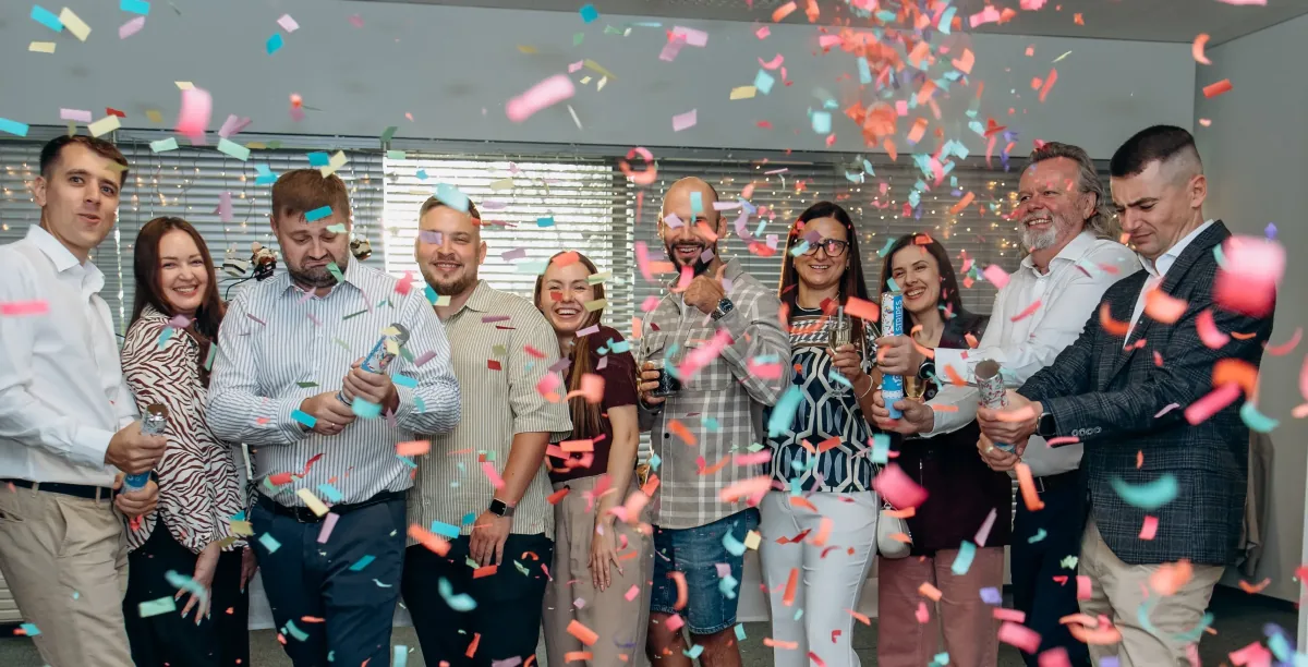 Group of colleagues celebrating with confetti poppers and glasses in an office