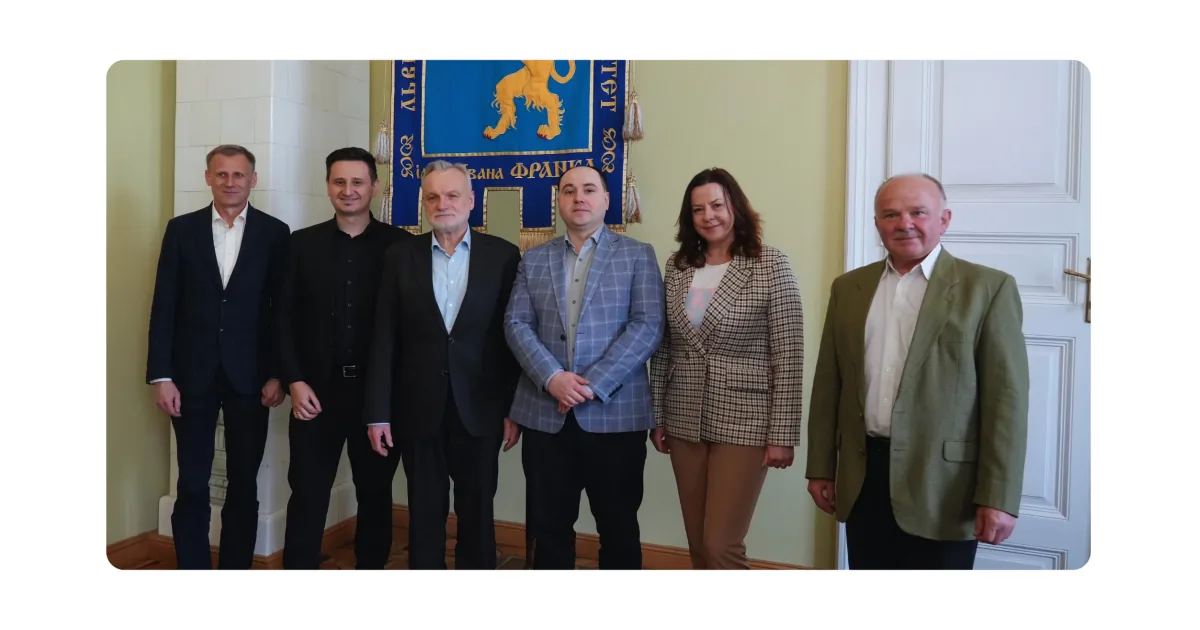 Six people in business attire posing in front of a Lviv University banner with a golden lion emblem