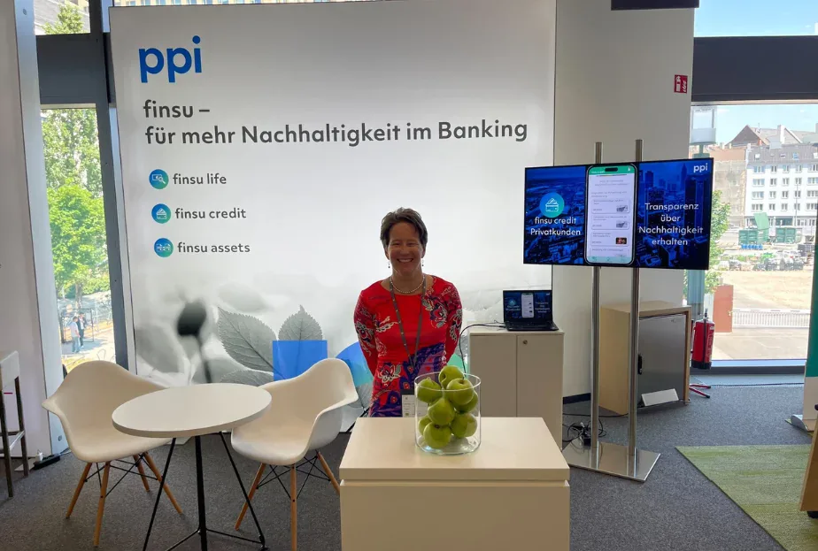 Exhibitor at a PPI booth promoting finsu sustainability banking products, with screens and a bowl of green apples