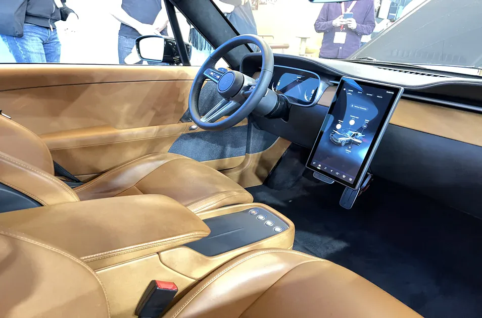 Car interior on display with tan leather seats, steering wheel and a large vertical touchscreen showing a vehicle app