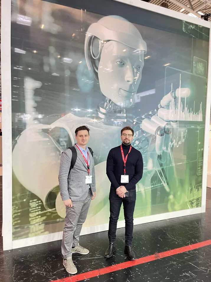 Two attendees with lanyards standing in front of a large humanoid robot graphic at electronica 2022