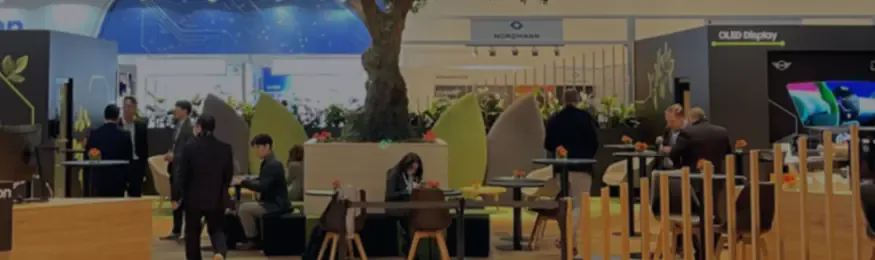 Dimmed view of an exhibition hall lounge with visitors at tables among planters and stands