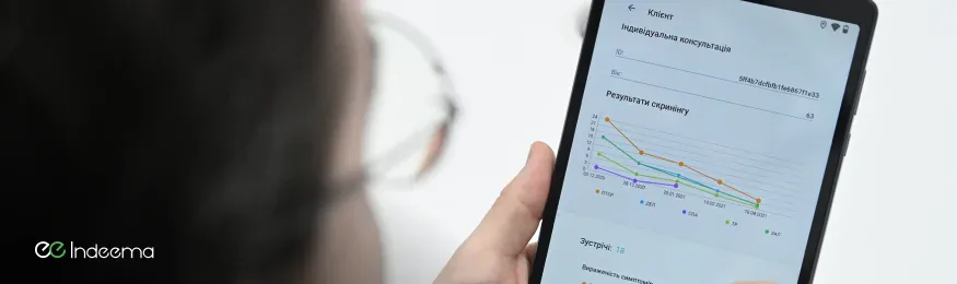 Hand holding a tablet with a Ukrainian-language app screen showing a client consultation and screening results chart