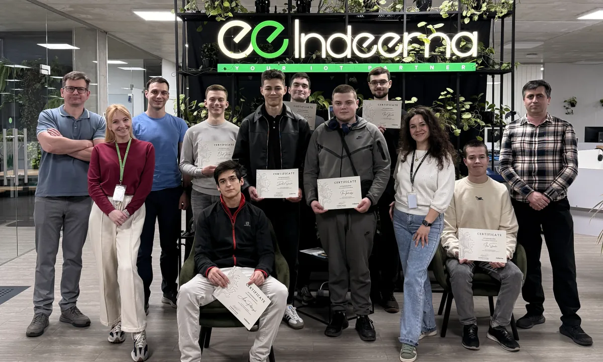 Group photo of participants, some holding certificates, in front of a lit Indeema Your IoT Partner sign