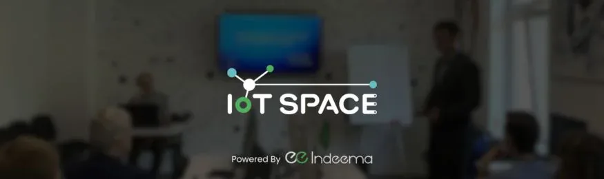 IoT Space logo with "Powered by Indeema" over a blurred photo of a presentation in a classroom
