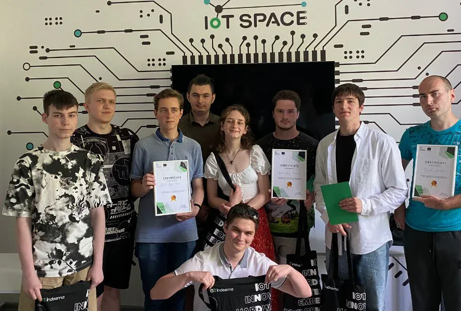 Students holding certificates and Indeema tote bags in front of the IoT Space circuit mural