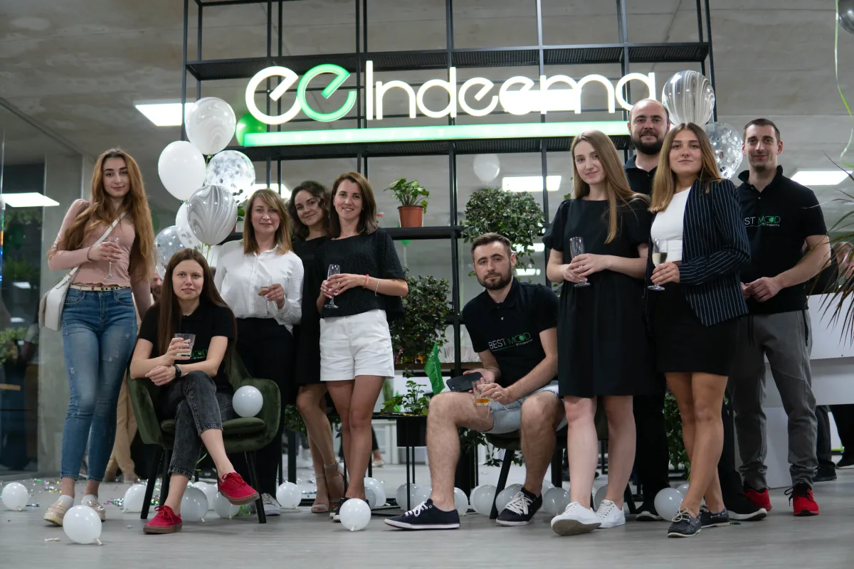 Indeema team members posing with glasses and balloons beneath an illuminated Indeema sign