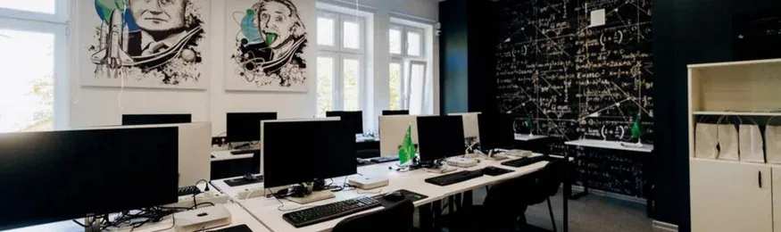 Students' IoT lab with rows of computer workstations, a formula-covered blackboard wall and portrait artwork