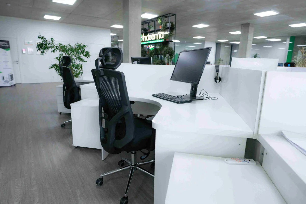 Empty white desk with a monitor, keyboard and black ergonomic chair, with the lit Indeema sign in the background