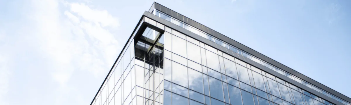 Low-angle view of a modern glass office building corner against a pale blue sky