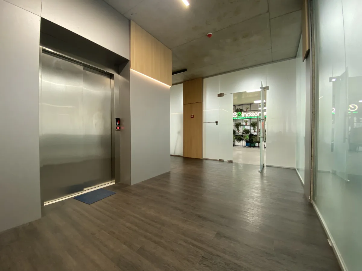 Hallway with a steel elevator door, wood flooring and a glass door opening onto the Indeema office with its lit sign