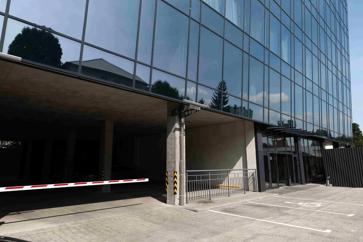 Glass facade of the office building with a parking barrier at the garage entrance and marked parking spaces
