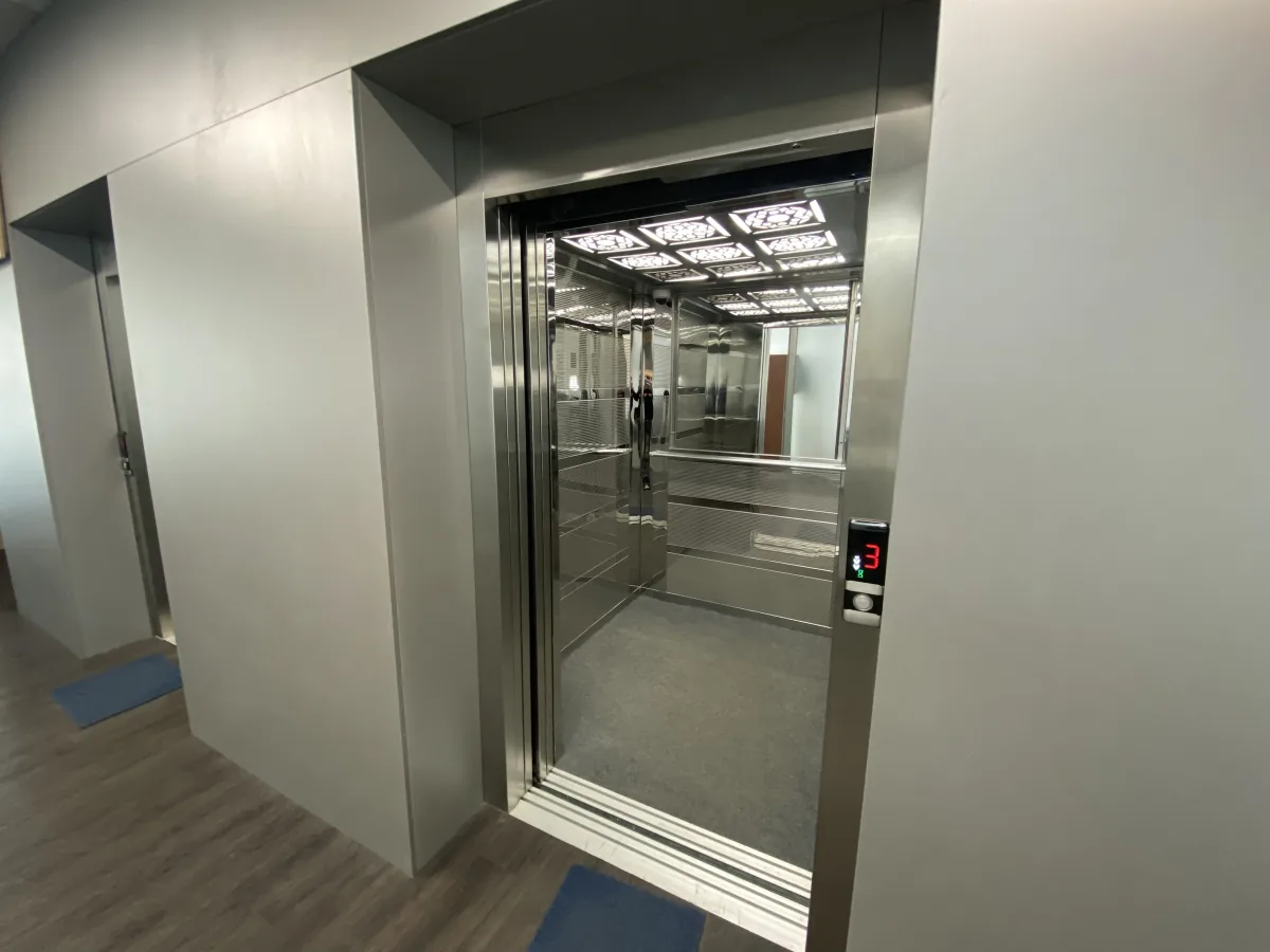 Open stainless steel elevator with a mirrored interior and patterned ceiling lights, floor indicator showing 3