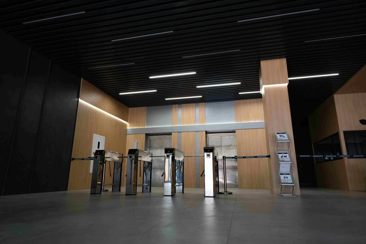 Building lobby with wood-panelled walls, a row of steel turnstiles and elevator doors behind them