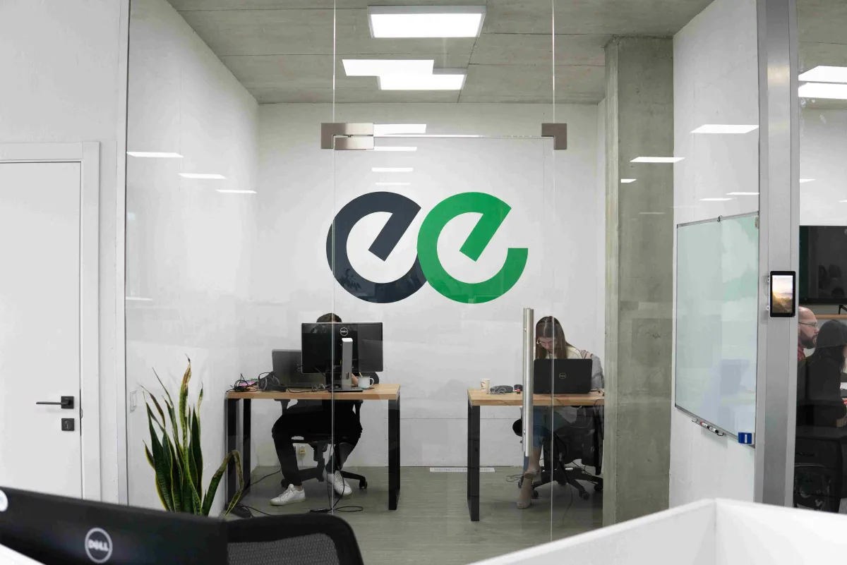 Glass-walled office room with the large Indeema logo on the wall and two people working at desks