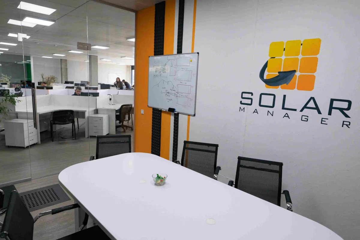 Meeting room with a Solar Manager logo on the wall, a whiteboard of diagrams and a white table, beside the open office