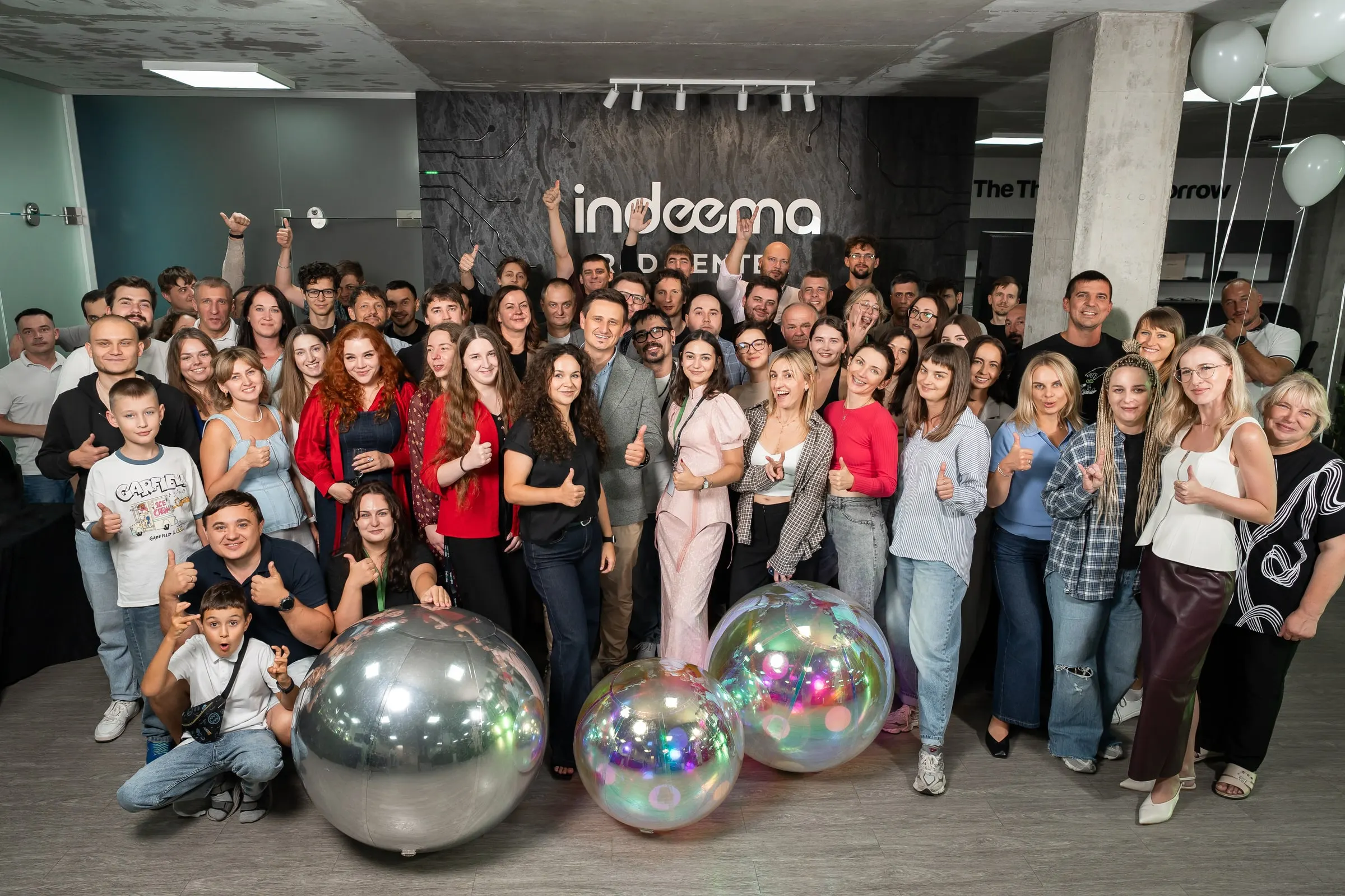 The Indeema team gathered in front of the Indeema R&D Center wall, many giving a thumbs-up.