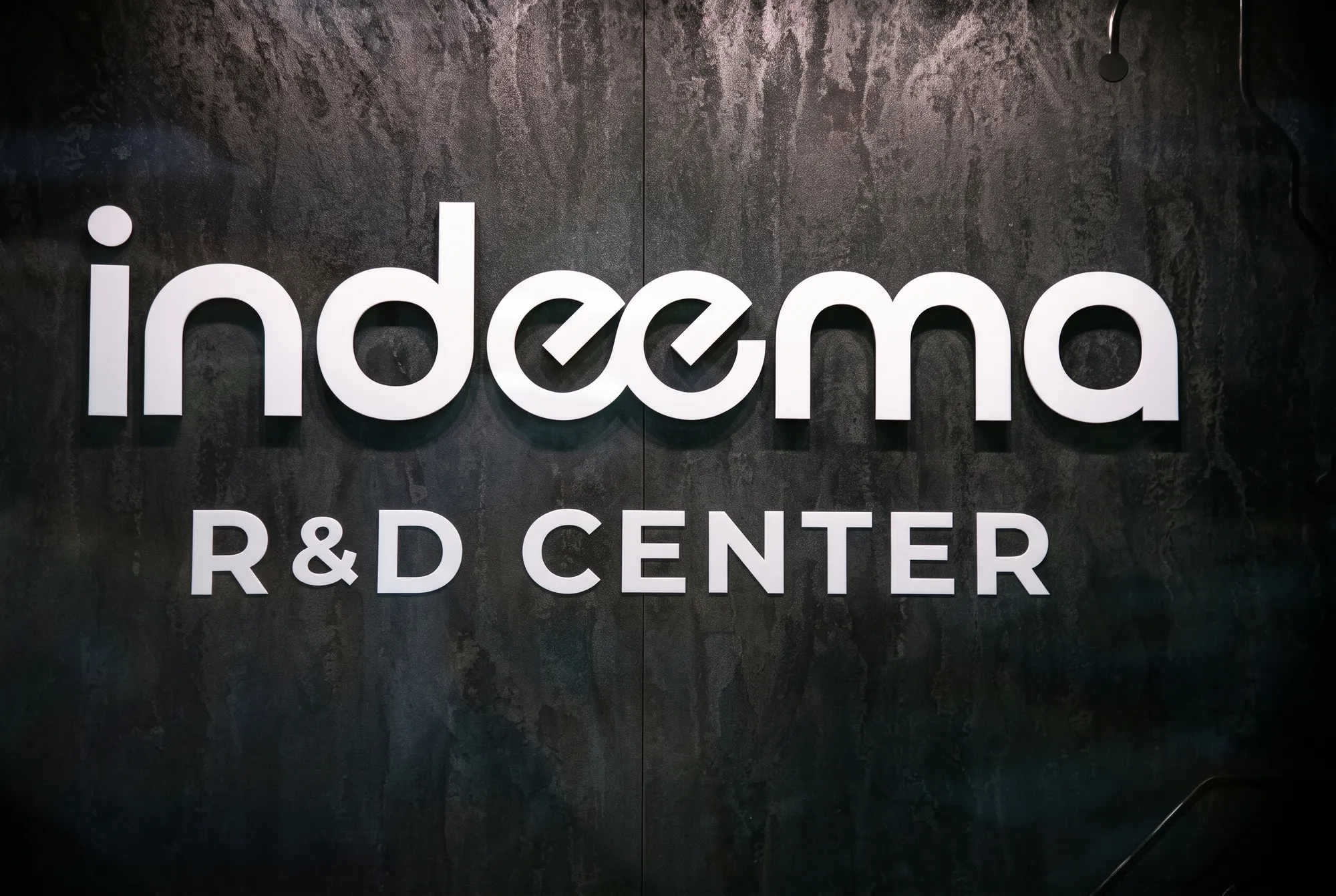 The Indeema R&D Center sign in metal lettering on a dark textured wall