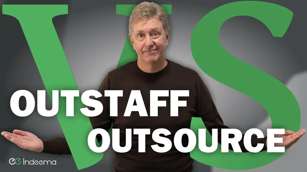 Video still: a presenter between the words Outstaff and Outsource on a large green VS