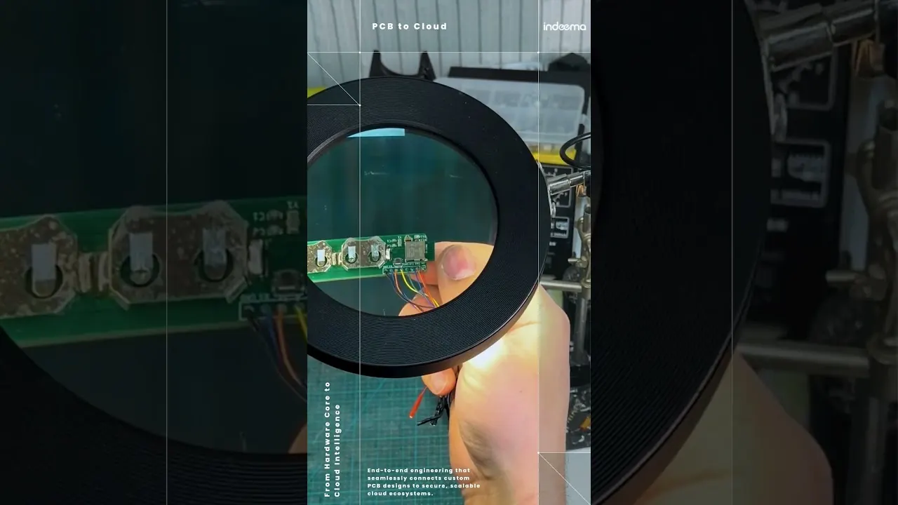 Video still: a hand holding a small green circuit board with soldered wires under a magnifying lens, titled PCB to Cloud
